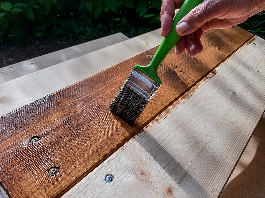 applying protective varnish on a patio wooden floor.painting woodwork outside.hand use brush paint clear lacquer on wood surface