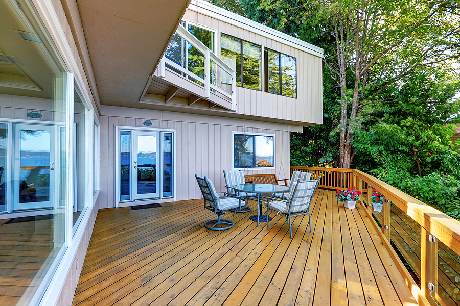 wooden walkout deck with outdoor table set and swinging bench. modern beige house exterior.