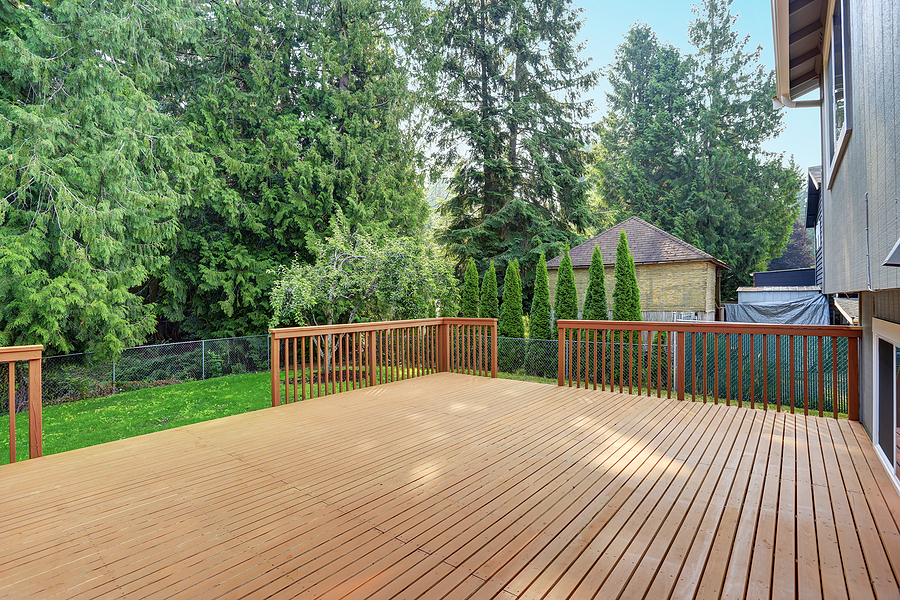 empty walkout deck boasts redwood railings overlooking well kept back yard.